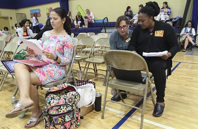 Using different methods and devices, Holy Spirit Preparatory School teachers (l-r) Whitney Wright, fourth grade, Leslie Hein, third grade, and Kathy Ann Nixon, fourth grade, get some work done in the gymnasium, while the students are away competing in the Battle of the Books semifinal round. Photo By Michael Alexander