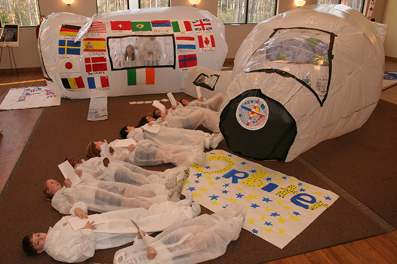 Members of the fifth-grade space orbiter crew demonstrate how they must lie on their backs inside the space shuttle until it launches. The nine-person crew of the orbiter joined the space station crew as they embarked on a 25-minute scripted mission before a group of second-graders and parents. Photo By Michael Alexander