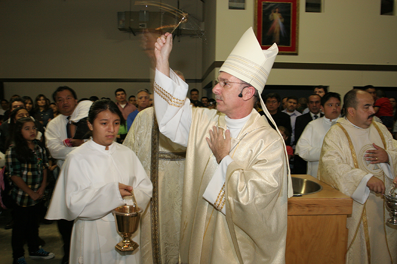 Bishop Luis Zarama makes his way around the mission sprinkling the congregation with holy water. Photo By Michael Alexander