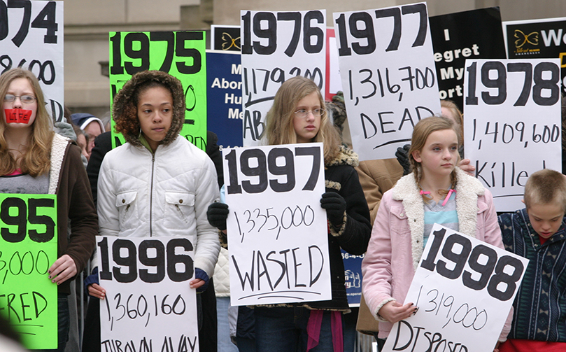 Young people and adults, each representing the 37 years since the legalization of abortion in the United States, hold their signs before the large crowd. Photo By Michael Alexander