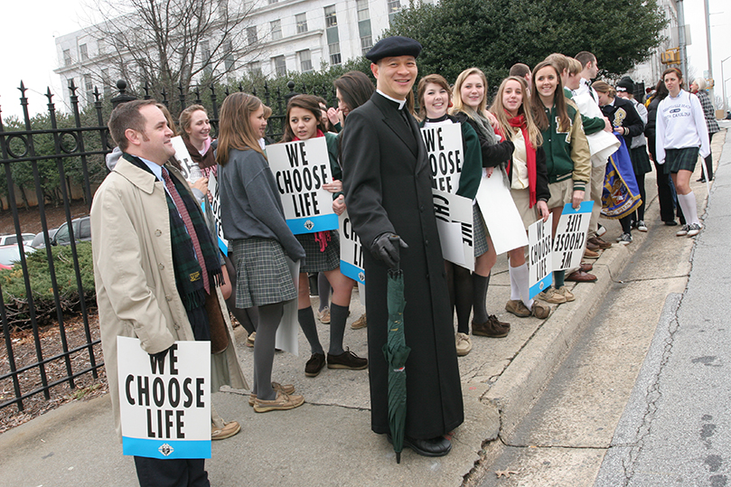 Blessed Trinity High School theology teacher Father Augustine Tran, center, and assistant principal Richard Martin, left, prepare to lead the 44 students who participated in the Together for Life Memorial Service for the Unborn back to the school bus. Photo By Michael Alexander