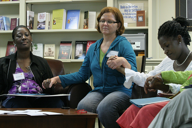 Roxanne Wilhelm, center, a retreat facilitator and a parishioner of St. Ann’s Church, Marietta, joins hands with retreatants Brenda Heath, left, and Tara Stallworth as they reflect during the closing moments of the retreat. Photo By Michael Alexander