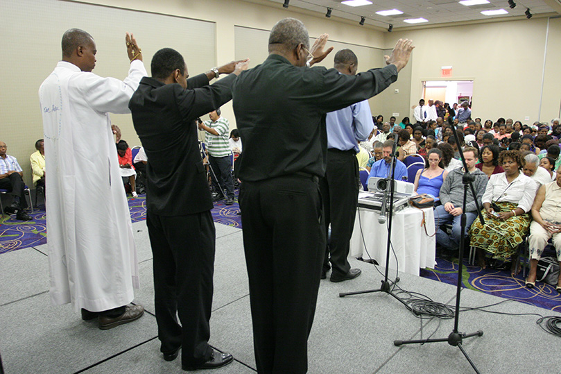 Father Guyma Noel, front of stage, is joined by (back row, l-r) visiting priest Father Jules Campion and archdiocesan priests Father Gilbert Exume, parochial vicar at St. Brigid Church, Johns Creek, and Father Jacques E. Fabre C S., administrator of San Felipe de Jesus Catholic Mission, Forest Park, as they pray over the attendees at the French Speaking Track. Photo By Michael Alexander