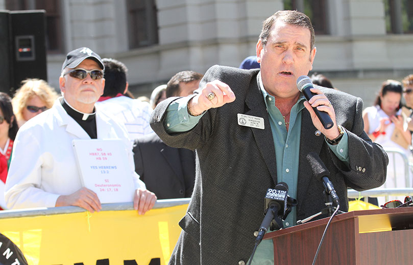 Pedro “Pete” Marin of District 96, who represents part of Gwinnett County, speaks with conviction and emotion as he stands before the immigration rally crowd. Participating in the background, left, is Jesuit Father Edward Salazar, a retreat director at Ignatius House Retreat Center. Photo By Michael Alexander