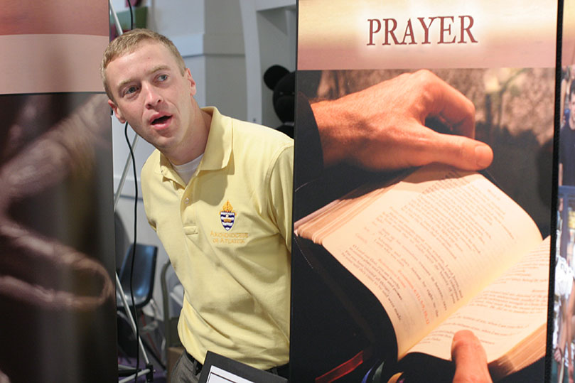 Michael Ferrin, associate director of the vocations office, looks down the hallway of the convention center as he peers around their booth's display. Photo By Michael Alexander