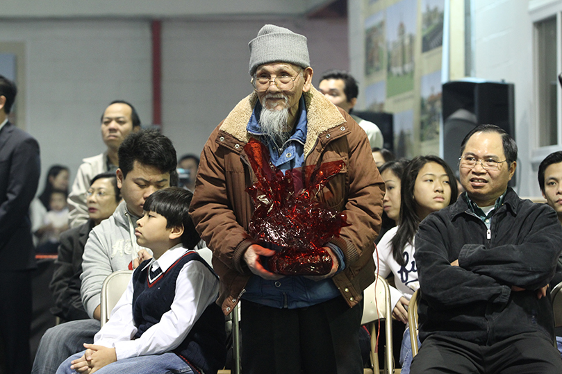 Lanh Van Quach, 84, is presented with a gift basket as church members, 80 years and older, were recognized. The baskets of fruit, rice cake and wine were brought up during the offertory procession. Photo By Michael Alexander