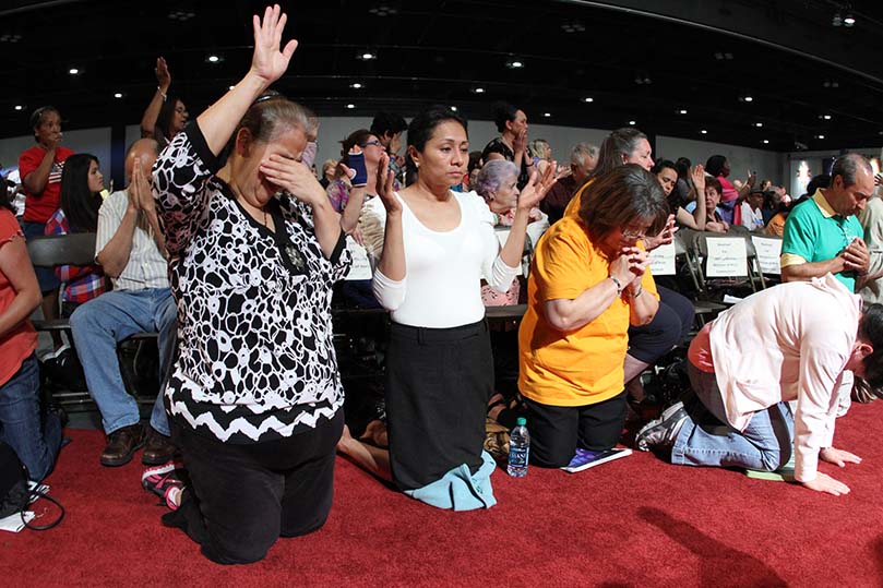 People down front fold and lift their hands in praise as Father Jack Durkin brings the Blessed Sacrament off the altar and among the congregation. Photo By Michael Alexander