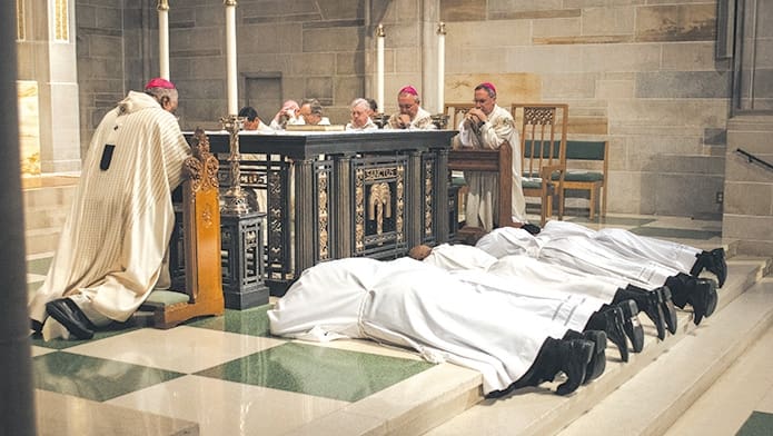 The five men being ordained as deacons in preparation for the priesthood lie prostrate in humility as the congregation prays for them. Archbishop Wilton D. Gregory, left, kneels along with the concelebrants of the Mass. (Photo by Thomas Spink/Archdiocese of Atlanta)