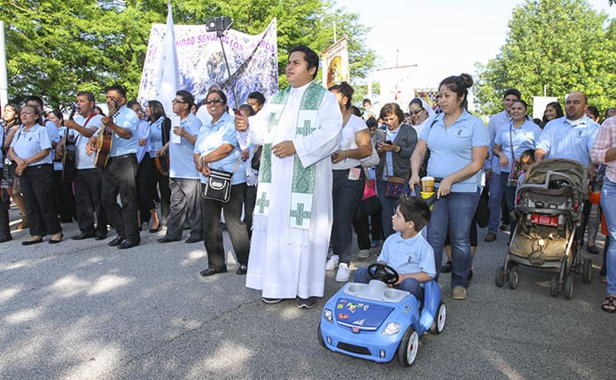 Holding a “selfie stick” in his right hand, Father Victor Cordoba-Gonzalez, center, parochial vicar at San Felipe de Jesus Mission, Forest Park, captures some video as he walks with a group of his parishioners during the morning Eucharistic Congress procession. Photo By Michael Alexander