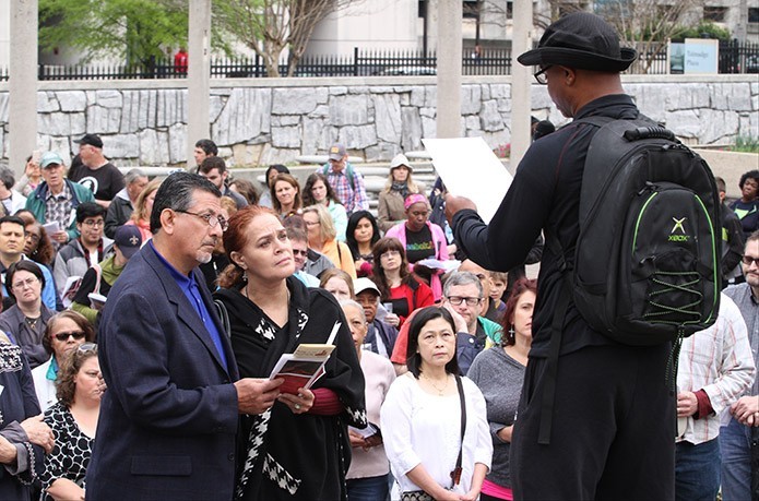 Good Friday Pilgrimage participants, like Michael and Dee Hidalgo, foreground left, listen at the second Station of the Cross (Jesus takes up his cross) as Joseph Barker II of St. Anthony of Padua Church, Atlanta, right, reads a reflection based on the theme of homelessness. Photo By Michael Alexander