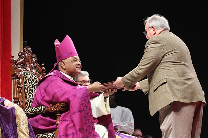 Archbishop Wilton D. Gregory, left, receives the Book of the Elect from Rafael Gaitan, a RCIA team member at Divino Niño Jesus Mission, Duluth, during the Feb.14 Rite of Election and the Call to Continuing Conversion at the Cobb Galleria Centre, Atlanta. The mission has 21 catechumens and 7 candidates this year. Photo By Michael Alexander