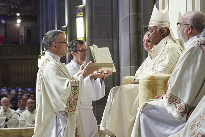 Archbishop Gregory presents the Book of Gospels to Deacon Erik Wilkinson. Deacon Wilkinson is assigned to serve at Immaculate Heart of Mary Church in Atlanta. Photo By Michael Alexander