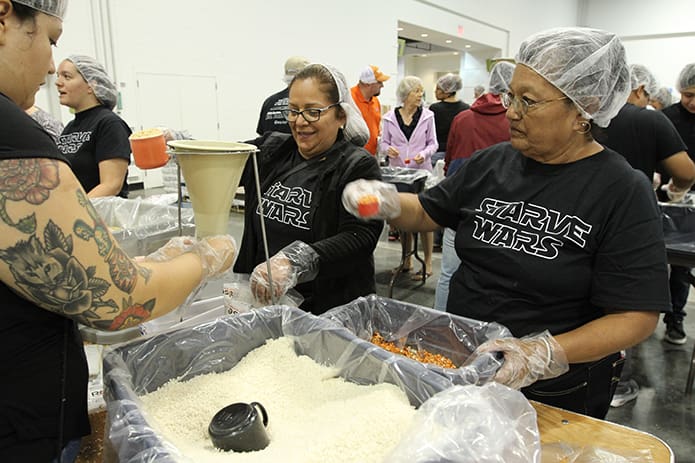 (Clockwise, from left) Maria Soto holds a meal bag under the funnel as Juana Gallegos prepares to pour in the soy and Silvestra Perez gets ready to add dehydrated vegetables. Photo By Michael Alexander