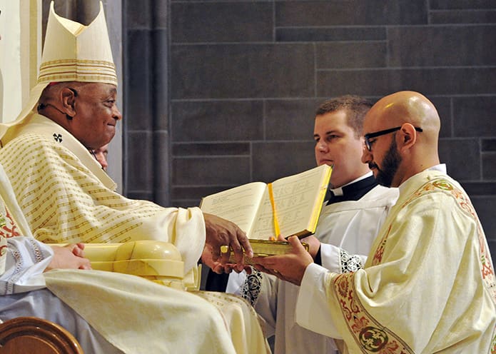 Archbishop Wilton D. Gregory presents the Book of the Gospels to Carlos Gustavo Ortega Valera as part of the rite of ordination.