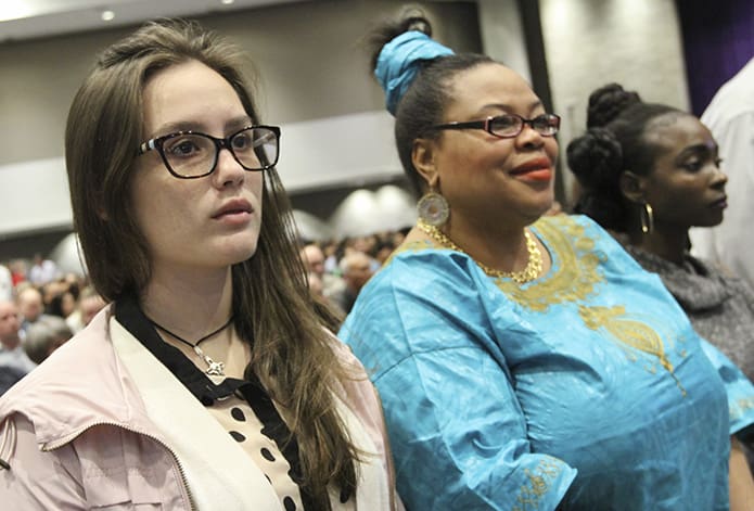 Victoria Minino, left and Deborah Alex, far right, catechumens from St. Benedict Church, Johns Creek, stand with others, during the presentation of catechumens in the Thomas Murphy Ballroom at the Georgia World Congress Center, Atlanta. Standing in the center is Alex’s godparent, Leticia Bertrand. Photo By Michael Alexander