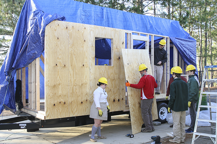 (Clockwise, from top right) Scott Findlay, business education teacher; Dr. Brent Hollers, project manager and business and technology education teacher; freshmen Matthew Stevens and C.J. Van Zant, and senior Rosie Nemec watch as Jason Podhorez, project manager and the school’s computer systems administrator, moves one of the exterior wall panels in place on the east side of the tiny home. Photo By Michael Alexander