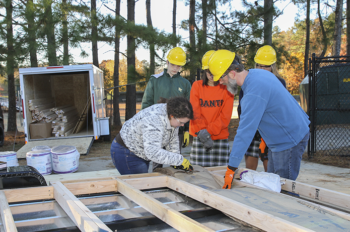 Senior Rosie Nemec, foreground left, cuts the insulation to fit properly between the wood beams of the sub-floor. Assisting from the right is Jason Podhorez, project manager and the school's computer systems administrator. Photo By Michael Alexander