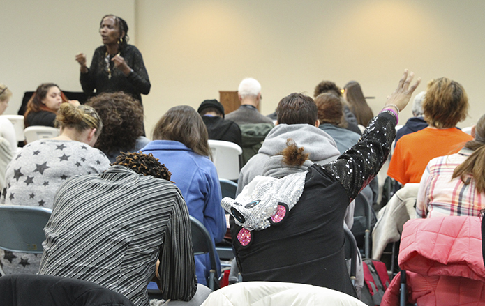 A woman in the foreground extends her arm out over the room, as Lucy Hall, standing, background left, the founder and CEO of Mary Hall Freedom House (MHFH), implores God to intercede on behalf of MHFH, as she leads those on hand in a final prayer. Mary Hall Freedom House has been in Sandy Springs since 1996. Photo By Michael Alexander