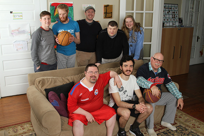 L'Arche Atlanta executive director Tim Moore, standing center, joins members of the community including (clockwise, from right seating position) core member Terry Hochschild; house assistant Grason Poling; core member Patrick Barlow; house assistant Lis Barrett; core member Corbin Allgood McKinnon; core member John Hudson and house assistant Kat Bailey for a March 20 photo at their Decatur home. Photo By Michael Alexander