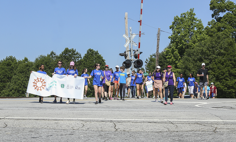 The group crosses the railroad tracks as they make their way to the Claredon Supermarket in Scottsdale, the third mile of their five-mile journey. Carrying the Share the Journey banner at this point are Marist School sophomores (l-r) Lauryn Walker, Christian Conte, Sara Jane Shulman and Clare Seymour. Photo By Michael Alexander