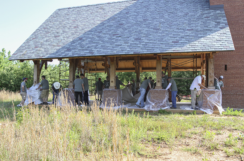 Nearly 20 seminarians and a lay volunteer from St. Brigid Church, Johns Creek, Ted Prenares, second from right, do the prep work on the Martin Gatins Chapel before they seal and stain the wood. It was one of the tasks undertaken during a May 16 seminarian workday on the natural burial grounds of Honey Creek Woodlands, Conyers. Photo By Michael Alexander