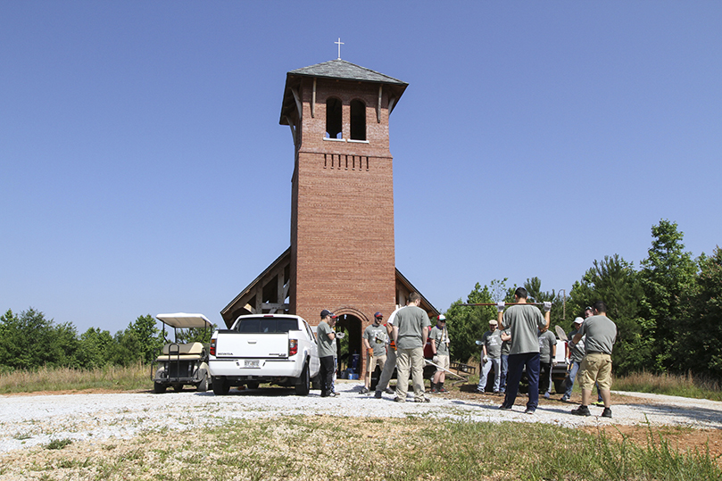 Seminarians gather the landscaping tools they will need for clearing brush and unwanted weeds around burial plots. Looming in the background is Martin Gatins Chapel, where another group of seminarians were sealing and staining its wood. Photo By Michael Alexander