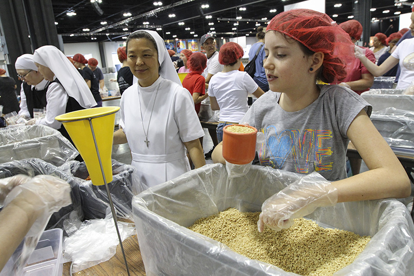 Salesian Sister of St. John Bosco Theresa Lee, left, a first time Starve Wars and Eucharistic Congress attendee, teamed up with nine-year-old Abby Wnek and two others, to form a meal packing crew. Sister Lee resides in Paterson, New Jersey, and Wnek is a member of St. Catherine of Siena Church, Kennesaw. Photo By Michael Alexander