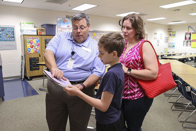 (L-r) Holy Redeemer middle school teacher Jerry Beck, left, goes over the class schedule with seventh-grader David Jimenez. Looking on is Jimenez’s mother Catherine. David, a student at the school since kindergarten, is the last of four Jimenez children to attend the Johns Creek Catholic school. Beck has been teaching for 31 years, and this is his 20th year at Holy Redeemer. Photo By Michael Alexander