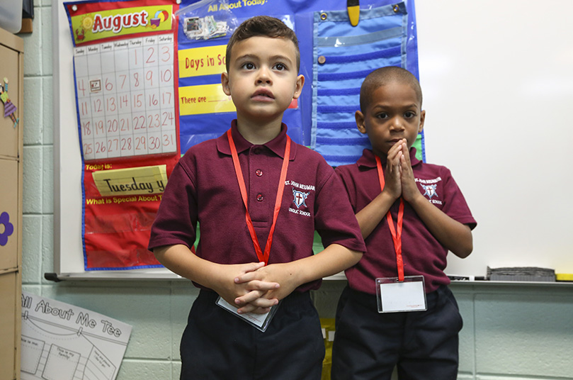 St. John Neumann Regional School kindergarten students Joshua Marquez, foreground, and Lanier Davis pause from socializing to participate in morning prayer with the other students in Joan Travis’ classroom, and in solidarity with students throughout the entire school. August 5 was the first day of school for St. John Neumann pupils. Photo By Michael Alexander