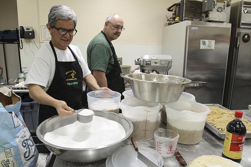 Humberto Guzman, president of the St. Oliver Plunkett Menâs Club, rations the appropriate portion of sugar and chopped walnuts, two of the several ingredients that go into the making of the walnut filling. Ken Drake, background, was responsible for combining all the ingredients in a bowl under the Hobart electric mixer. Photo By Michael Alexander