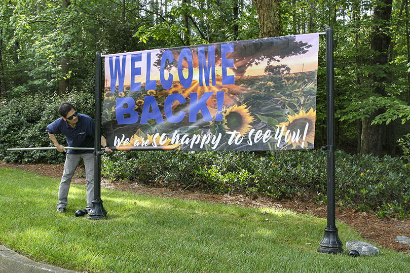 Khanh Mai, the facilities manager at St. Benedict Church, hangs one of two banners, 8 feet by 4 feet, greeting parishioners at the entrance to the Johns Creek parish. St. Benedict Church resumed its first public Mass on Monday, May 25. Their regular worship schedule took effect on Tuesday, May 26. Photo By Michael Alexander