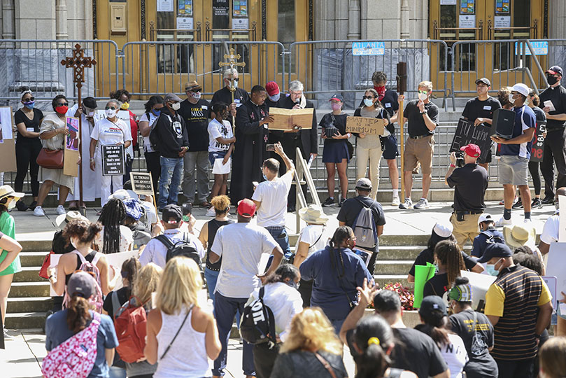 After a Bible reading from the Book of Amos by Father Urey Mark, left center, holding the book, Bishop Bernard E. Shlesinger III, right center, leads a litany of forgiveness on the steps of Atlanta City Hall, the first stop during the Catholic march for racial justice through downtown Atlanta. Father Mark serves as chaplain at Lyke House, the Catholic Center at Atlanta University. Photo By Michael Alexander