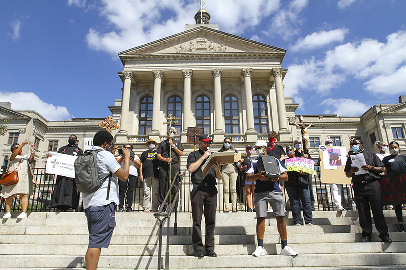 Transitional deacon, Rev. Mr. Paul Porter, holding book, recites a responsorial psalm from the steps of the Georgia State Capitol, the second stop during the Catholic march for racial justice through downtown Atlanta. Photo By Michael Alexander