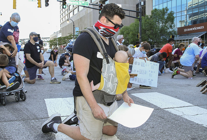 With his four-month son, Walt, strapped to his chest, Robert Sabbath takes a knee during a moment of silence for 8 minutes and 46 seconds in the street beside Centennial Olympic Park. It represented the length of time 46-year-old, handcuffed George Floyd was pinned to the ground, at the neck, under the weight and knee of Minneapolis police officer Derek Chauvin before he died on May 25. Photo By Michael Alexander