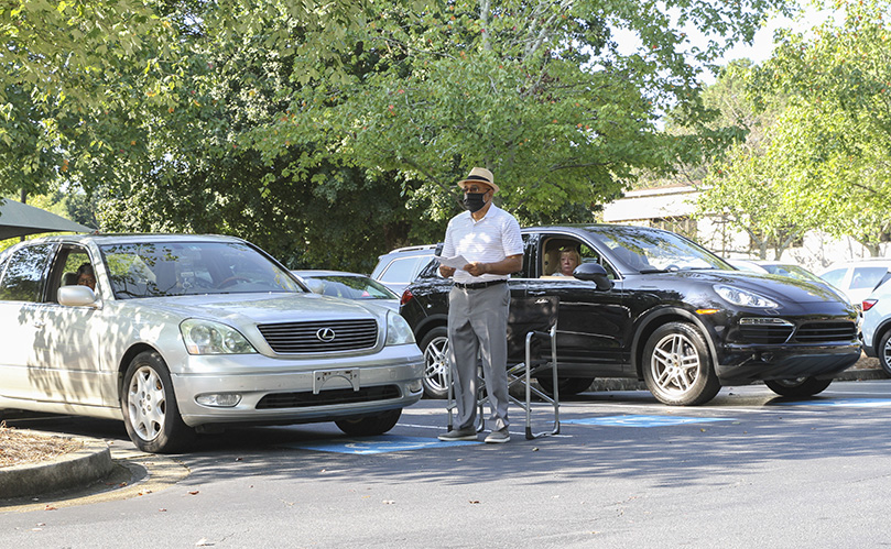 Tim Hart participates in the liturgy from outside his vehicle, as his wife, Lucretia, left, watches and listens from inside their car. Those who choose to hear the Mass from their automobiles can tune in to 102.7 FM. Photo By Michael Alexander