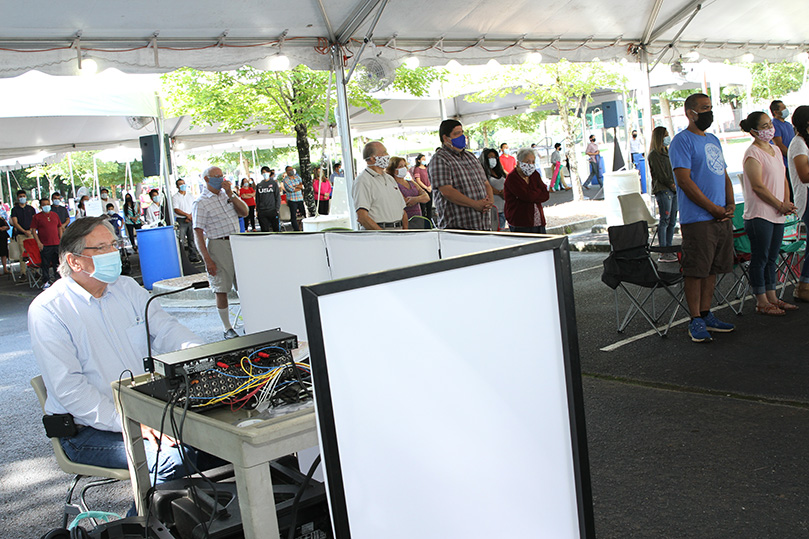 Michael Weglarz, seated, foreground left, serves as the sound technician for the Sunday outdoor Masses at St. Thomas Aquinas Church. Photo By Michael Alexander