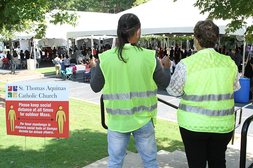 Ushers and spouses, Moses and Patricia Abreu join hands during the Our Father at the outdoor Spanish Mass at St. Thomas Aquinas Church, Atlanta. Photo By Michael Alexander