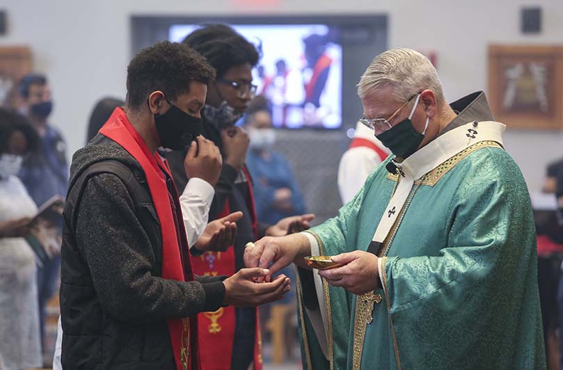 Christian Boothman, foreground left, one of three catechumens who were baptized and confirmed, receives holy Communion from Archbishop Gregory J. Hartmayer, OFM Conv. Boothman is a junior political science major at Georgia State University. Photo By Michael Alexander