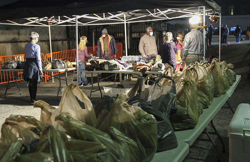 Socially distanced and two at a time, clients approach the tent beside the Shrine of the Immaculate Conception, Atlanta, where they are given bags containing dinner, breakfast and lunch. Also included are foil blankets, hats, masks, rain ponchos, socks and hand and foot warmers. Winter coats and jackets are available upon request. The Central Night Shelter has extended its services to homeless and marginalized members of the community since 1980. Photo By Michael Alexander