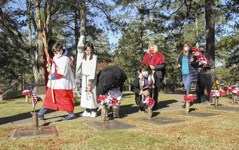 Nine-year-old altar server Gabriel Muller and 12-year-old server Lily Grace lead people around the inner and outer circle of the Calvary section at Sandy Spring’s Arlington Memorial Park. Participants went to each grave of a priest and bishop as their names were called out. Altogether they placed poinsettias on 51 graves the morning of Dec. 5. Photo By Michael Alexander