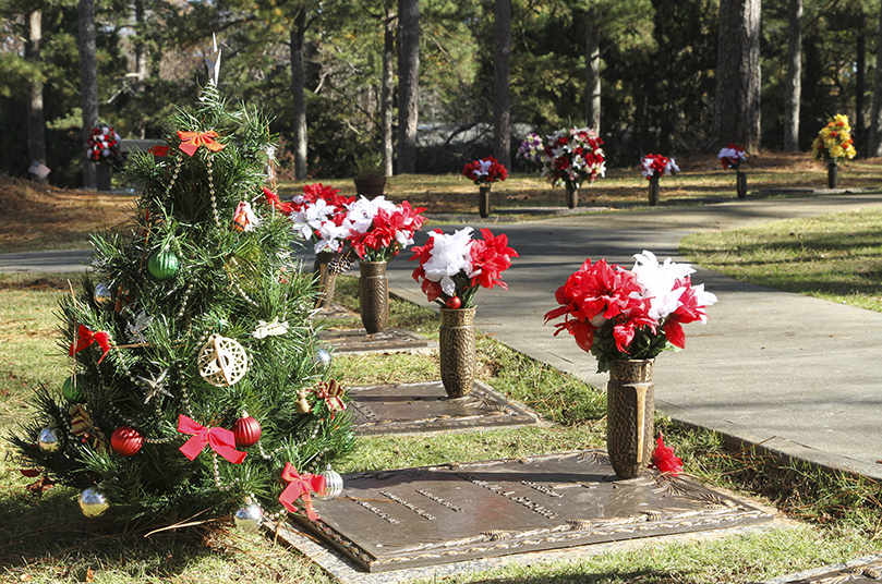 Poinsettias were carefully placed on the graves of deceased clergy from the Archdiocese of Atlanta, like that of the late Father Austin Fogarty, foreground by Christmas tree, who died in 2014. A contingent of some 15 Catholics took the morning of Dec. 5 to honor the clergy who had died between 1960 and 2020. Photo By Michael Alexander