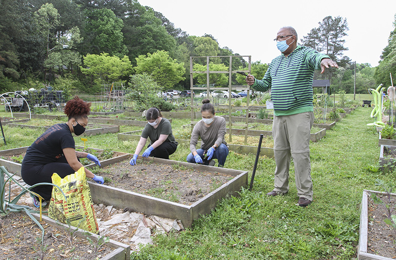 Master Gardener and Corpus Christi Church parishioner Columbus Brown, standing right, provides some instructions and shares some information about the Stone Mountain Community Garden. He was addressing some volunteers who came to work at the garden on April 17. The volunteers (clockwise, from left) included Ashlynn Maxey, Kristin McKenna and Sora Shim. Photo By Michael Alexander