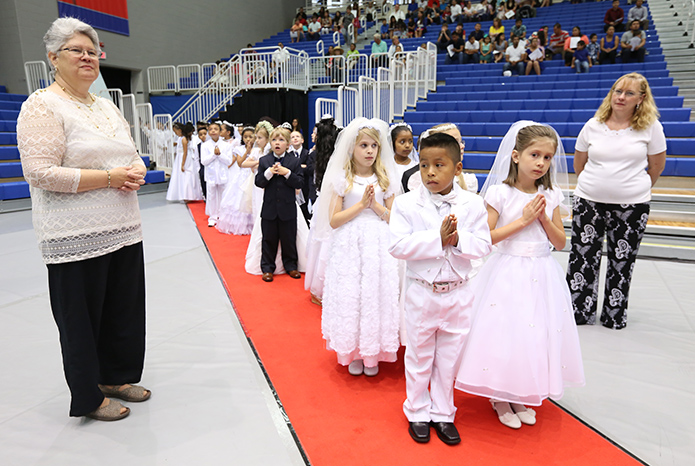 Standing in the front of the processional line, 8-year-old Michael Gonzalez, left, and 7-year-old Emma McWhorter prepare to lead the group of first communicants to their seats. Standing with them are Debbie Ginther, left, second grade Sunday school teacher, and parent volunteer Margaret Tatro. Photo by Michael Alexander