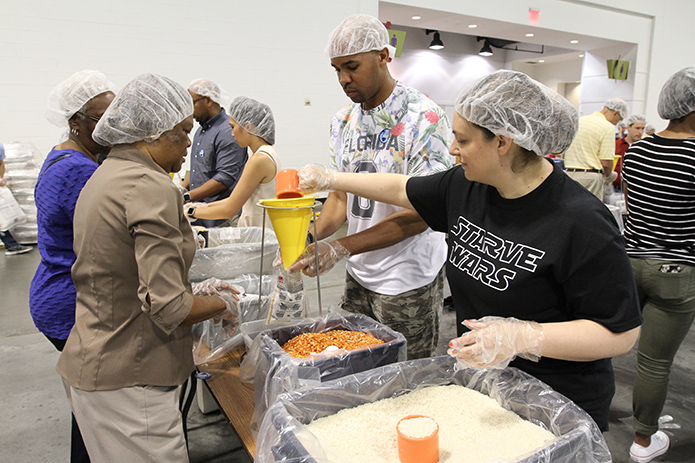 (Clockwise, starting second from right) Erik Newby of St. Anthony of Padua Church, Atlanta, holds a meal bag under the funnel as Mary Suazo of St. Lawrence Church, Lawrenceville, pours rice into the meal bag, while Marian Corbin and Susanna Williams of Most Blessed Sacrament Church, Atlanta, round out their four-person meal packing team. Some 150 people participated in the first of two June 3 shifts for Starve Wars at the Georgia International Convention Center, College Park. Photo By Michael Alexander