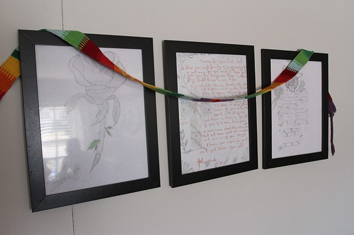 Artwork and a handwritten note of thanks from a detainee are displayed on a wall in the hospitality house’s living room. In the corner of the nearest drawing, written in Spanish are the words “Dios te bendiga” (God bless you). Photo By Michael Alexander