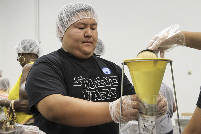 Thien Pham of the Holy Vietnamese Martyrs Church, Norcross, holds a meal bag under the funnel as one of his meal packing team members pours in a cup of dehydrated soy. The other three items added to the bag include dehydrated vegetables, a vitamin and mineral packet and rice. Photo By Michael Alexander