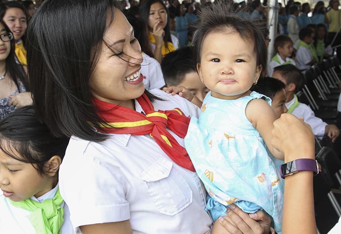 Charity Nguyen, right, extends a hand to those around her during the sign of peace as her mother, Thao, a youth leader for the parish’s Eucharistic Youth Movement looks on. Charity turned 1 on Sept. 2. Photo By Michael Alexander