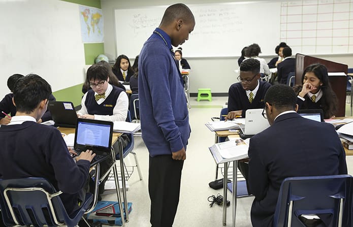 Brandon Render, standing center, human geography teacher at Cristo Rey Atlanta Jesuit High School, observes some of his students as they tackle an assignment in his morning classroom. Photo By Michael Alexander