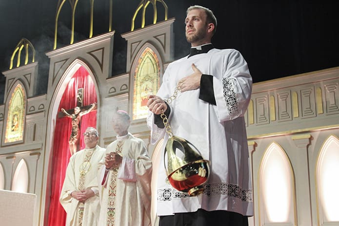 Archdiocese of Atlanta seminarian Joe Wagner swings the censor left and right as the Gospel is read from the Book of Mark during the closing Mass of the Eucharistic Congress. Standing in the background are Bishop Robert Barron, left, the auxiliary bishop of Los Angeles, Calif., and Bishop John Do Van Ngan, the auxiliary bishop of Xuân Lôc in Vietnam. Photo By Michael Alexander