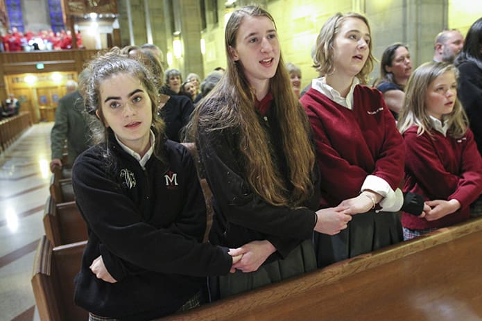 As the Cathedral Choir of Christ the King, under the direction of choirmaster Kevin Culver, leads the congregation during the closing hymn, “We Shall Overcome,” (l-r) Our Lady of Mercy High School freshman Danielle Garger, seniors Candace Todd and Anna Pitstick, and freshman Sophia Launay-Fallasse join hands during the singing of the old civil rights anthem. Photo By Michael Alexander